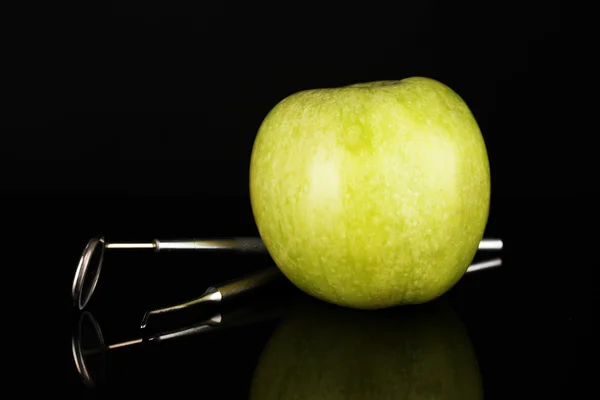 Green apple and dental tools isolated on black