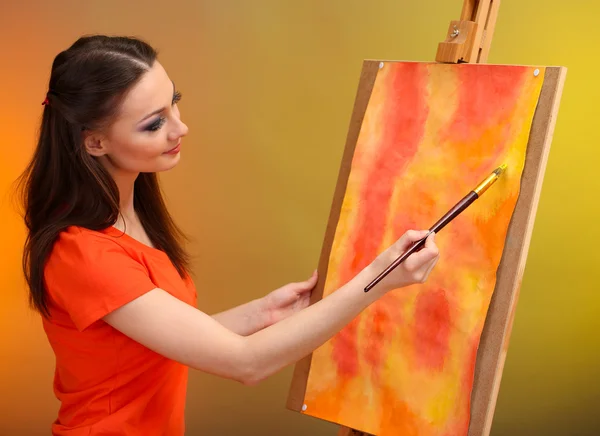 Beautiful young woman painter at work, on bright color background
