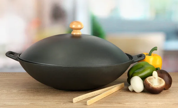 Black wok pan and vegetables on kitchen table, close up