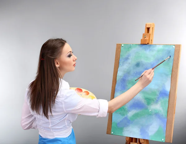 Beautiful young woman painter at work, on grey background
