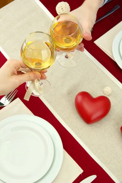 Hands of romantic couple toasting their wine glasses over a restaurant table