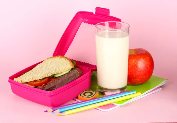 Lunch box with sandwich,apple,milk and stationery on pink background