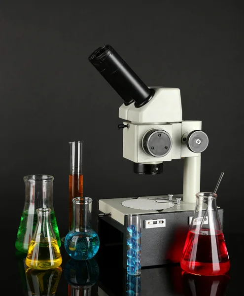 test tubes with colorful liquids and microscope on dark grey background