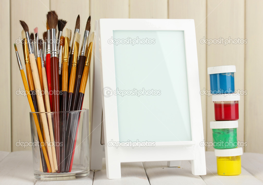 Photo frame as easel with artist's tools on wooden background - Stock 