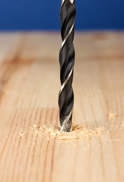 Close-up image of drilling hole on wooden plank, on color background