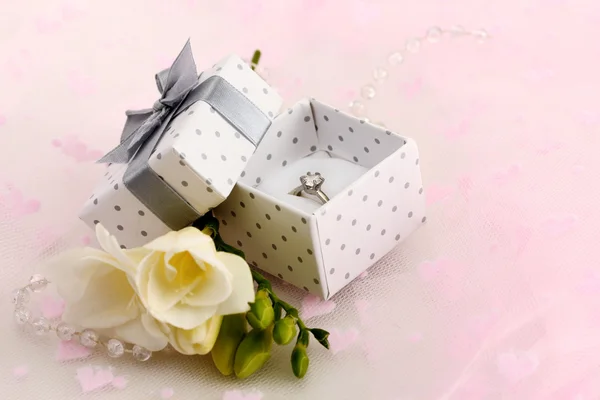 Beautiful box with wedding ring and flower on pink background