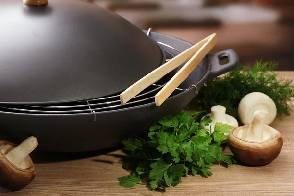 Black wok pan and mushrooms on kitchen wooden table, close up