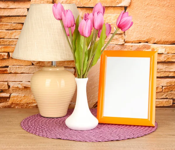 Colorful photo frame, lamp and flowers on wooden table on stone wall background