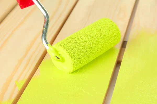 Paint roller brush with green paint, on wooden background