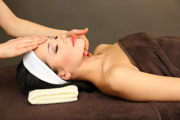 Beautiful young woman in spa salon taking head massage, on dark background