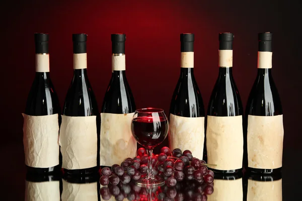 Composition of wine bottles, glass and grape, on dark red background