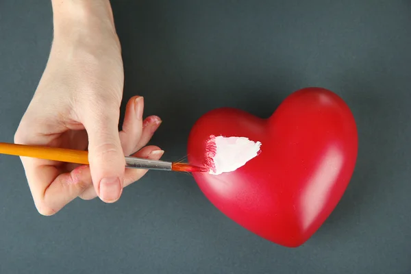 Hand paints white spot on heart, on color background. Conceptual photo treatment of heart disease.