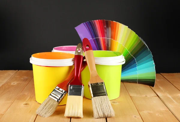 Paint pots, paintbrushes and coloured swatches on wooden table on dark purple background
