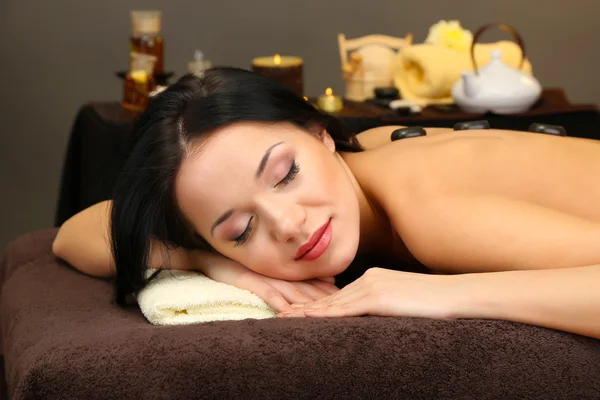 Beautiful young woman in spa salon with spa stones, on dark background