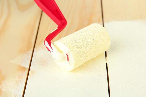 Paint roller brush with white paint, on wooden background