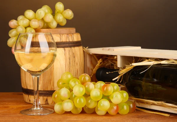 Wooden case with wine bottle, barrel, wineglass and grape on wooden table on brown background