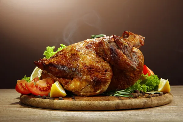 Whole roasted chicken with vegetables, on wooden table, on brown background