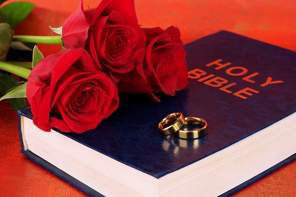 Wedding rings with roses on bible on red background