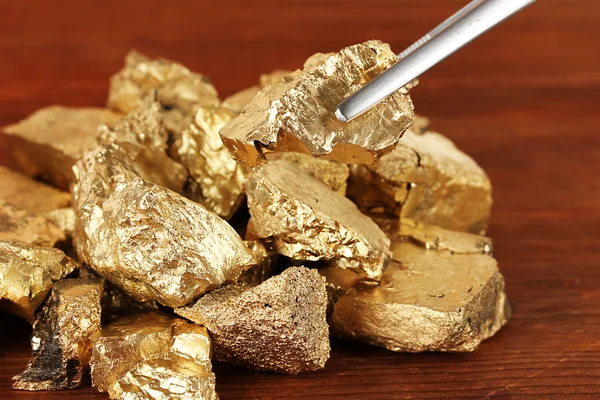 Tweezers holding golden nugget on wooden background