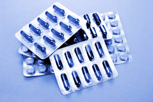 Capsules and pills packed in blisters in blue light on blue background