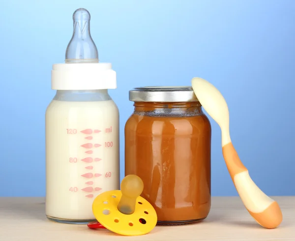 Baby food, bottle of milk and puree on blue background