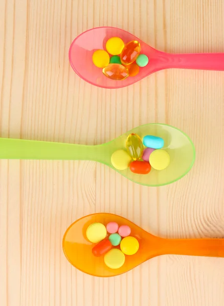 Plastic spoons with color pills on wooden background