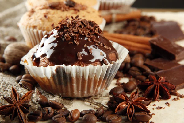 Tasty muffin cakes with chocolate, spices and coffee seeds, on beige background