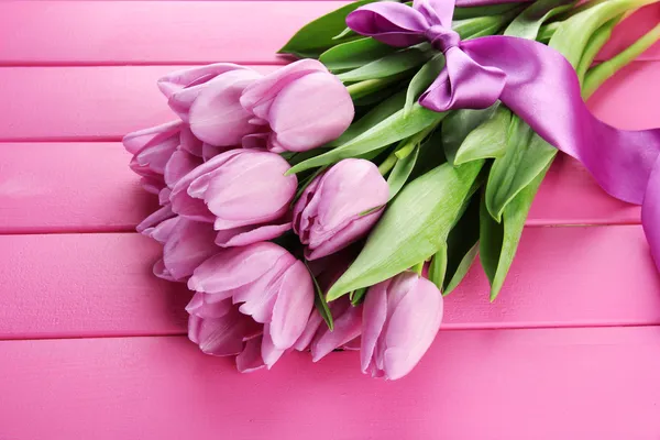 Beautiful bouquet of purple tulips on pink wooden background