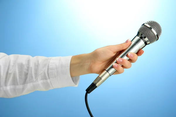 Female hand with microphone, on blue background