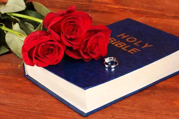 Wedding rings on bible with roses on wooden background