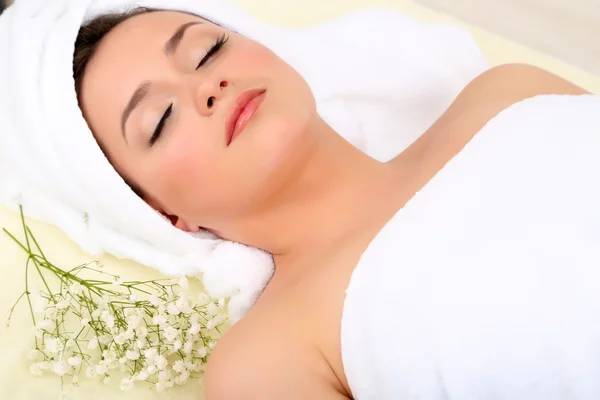 Beautiful young woman lying in spa salon with flowers close up