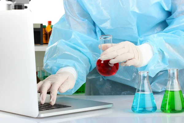 Scientist entering data on laptop computer with test tube close up