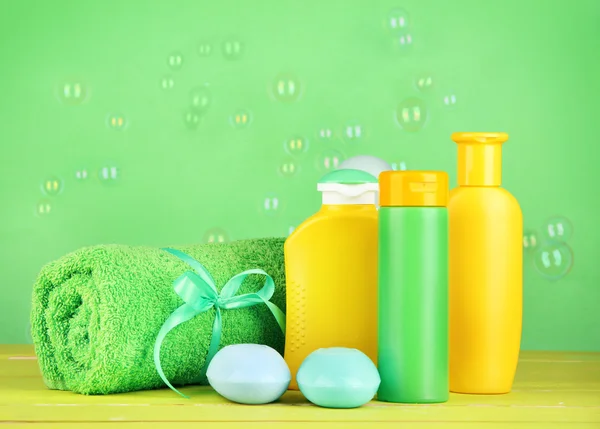 Baby cosmetics, towel and soap on wooden table, on green background