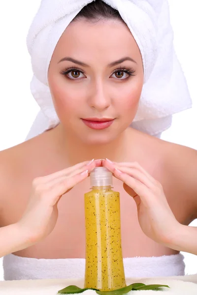 Beautiful young woman with towel on her head and bottle of cream with scrub isolated on white