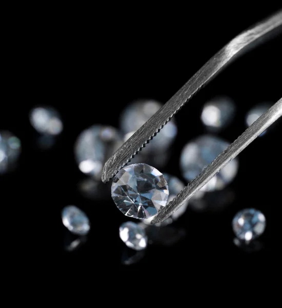 Beautiful shining crystal (diamond) in the tweezers, on black background