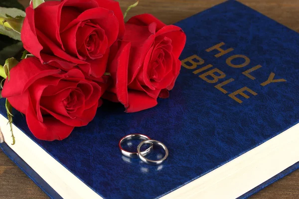 Wedding rings on bible with roses on wooden background