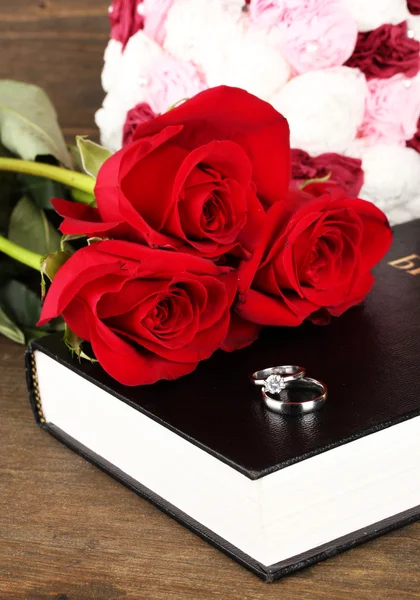 Wedding rings on bible with roses on wooden background