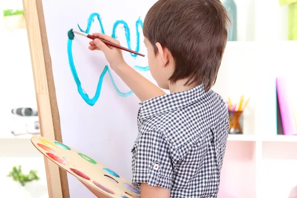 Little boy painting paints picture on easel