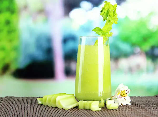 Glass of celery juice, on bamboo mat, on green background