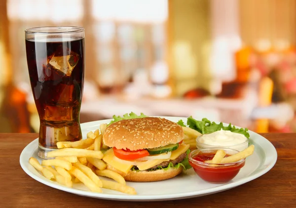 Tasty cheeseburger with fried potatoes and cold drink, on bright background