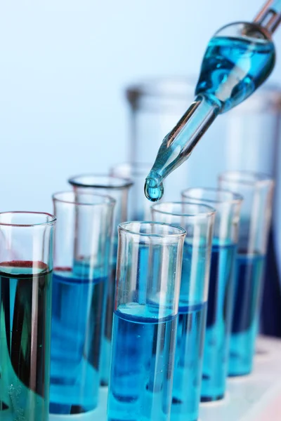 Laboratory pipette with drop of color liquid over glass test tubes, close up