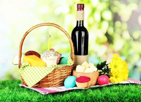 Easter basket: Conceptual photo of traditional easter food in wicker basket, on green grass, on bright background