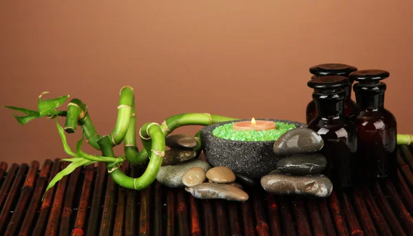 Still life with green bamboo plant and stones, on bamboo mat on color background