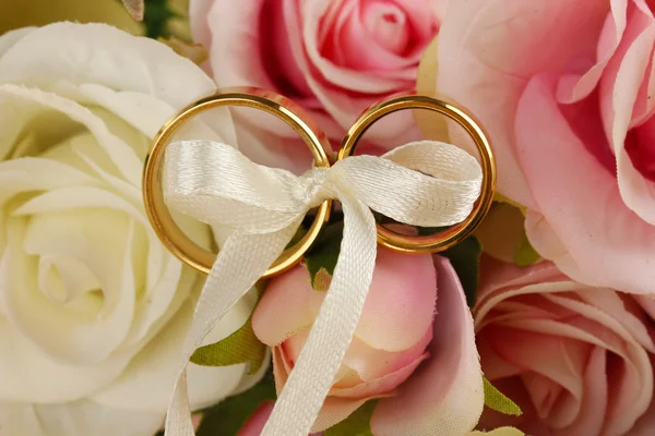 Wedding rings tied with ribbon on rose background