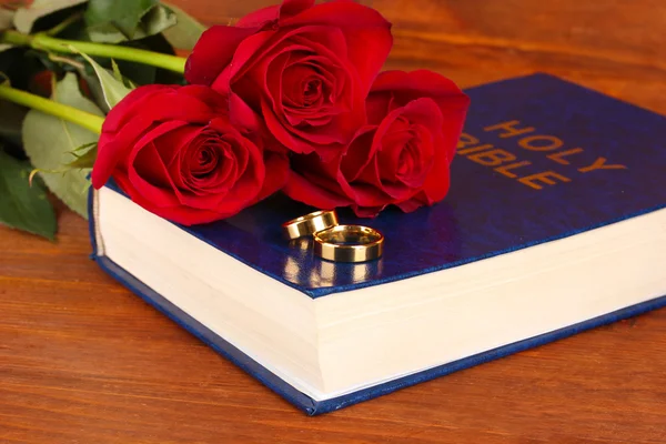 Wedding rings on bible with roses on wooden background