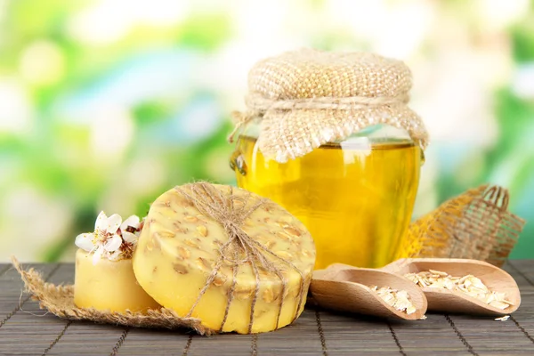 Hand made soap and ingredients for soap making on bamboo mat, on green background