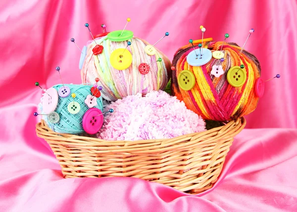 Colorful buttons and multicolor wool balls in wicker basket, on color fabric background