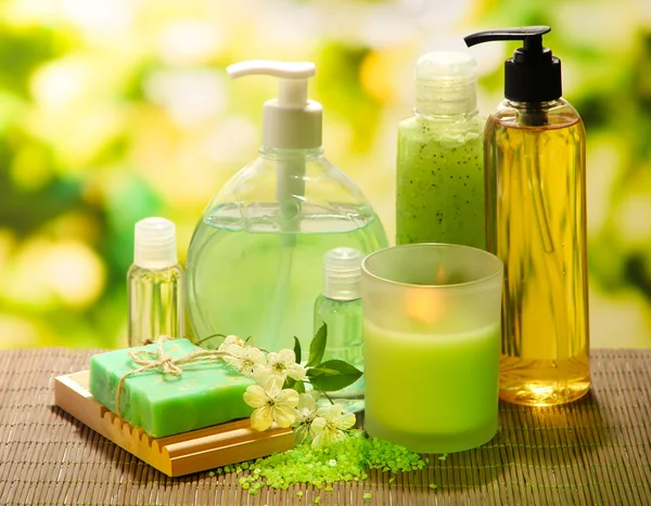 Cosmetics bottles and natural handmade soap on green background