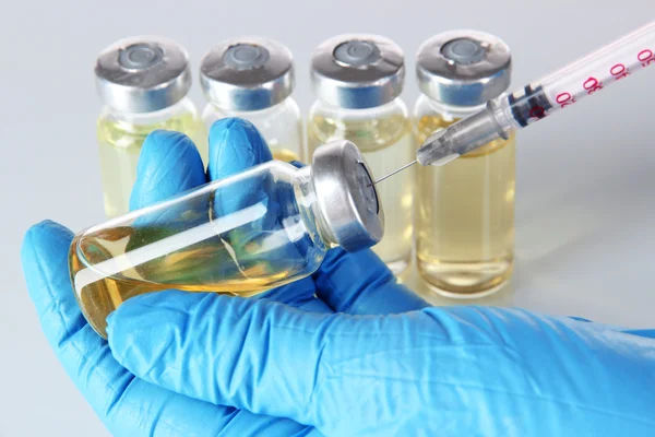 Medical bottles and syringe in hand on gray background