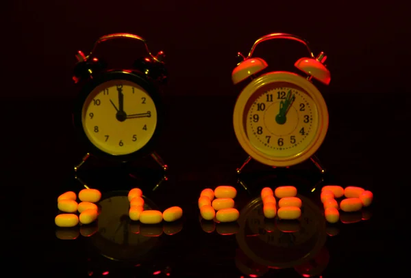 Old style alarm clocks and pills, on dark background